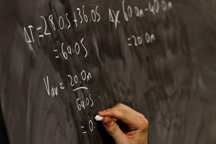 hand doing math equations on chalk board