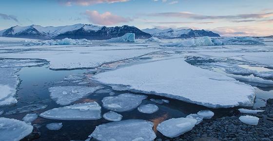 Stock photo of arctic ice sheets breaking apart over water. In the distance are icy mountains.
