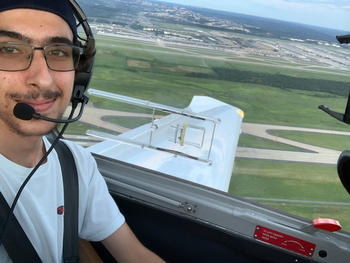 Male student in the SEOR department at Mason wears glasses, headset while sitting in a cockpit of a plane in the sky.