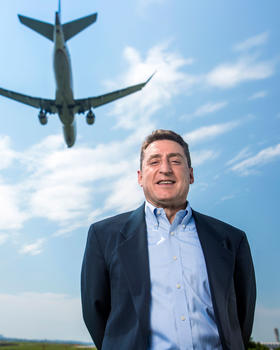 A man stands in front of a plane, flying overhead